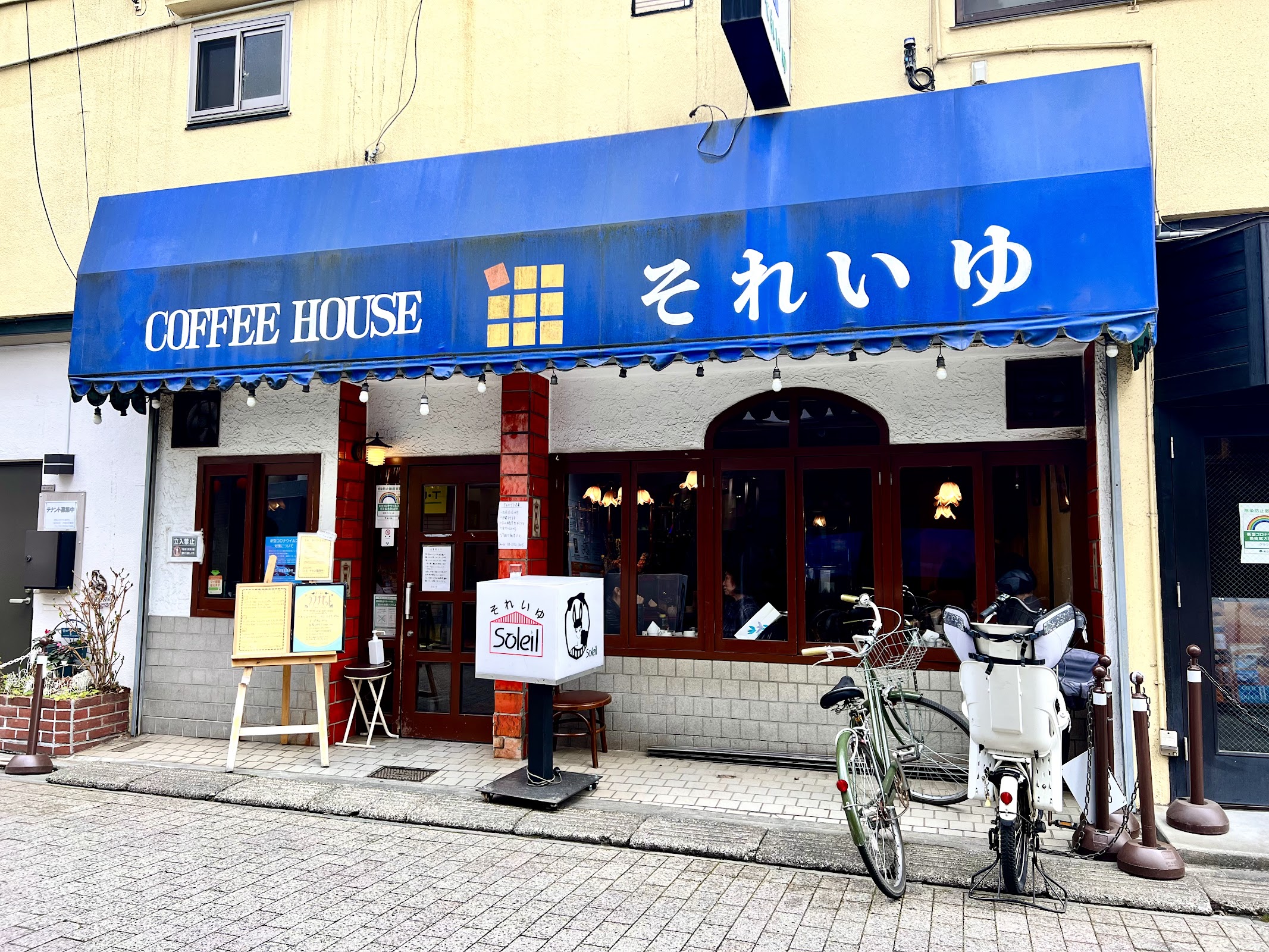 青いひさしに白抜きで「COFFEE HOUSE それいゆ」と書かれた外観、店頭の白いSoleil看板と自転車