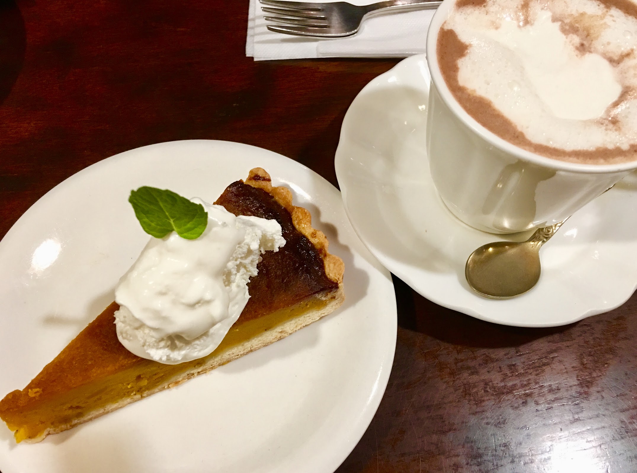 白い丸皿に盛られたかぼちゃパイのスライスとホイップクリーム、隣に泡立ったカプチーノのカップとソーサー